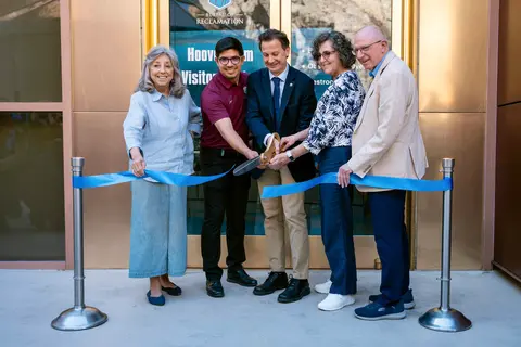 Five people cut a blue ribbon in front of a building.