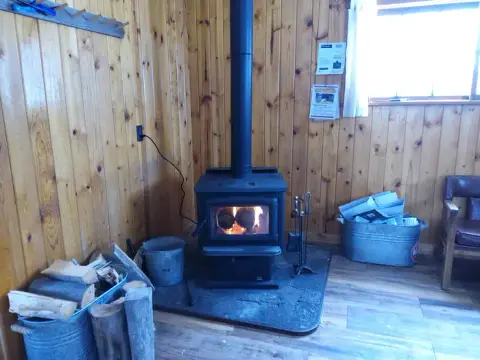 A wood burning stove sits in the corner of a room with wood paneled walls.