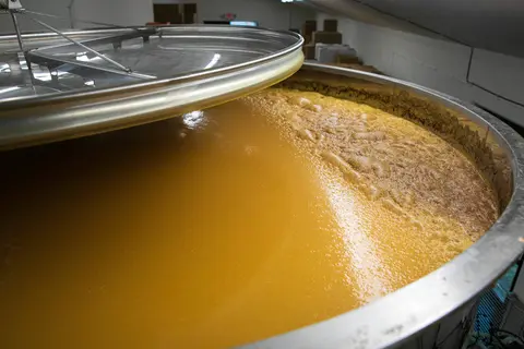An open stainless steel vat filled with liquid during production inside a facility.