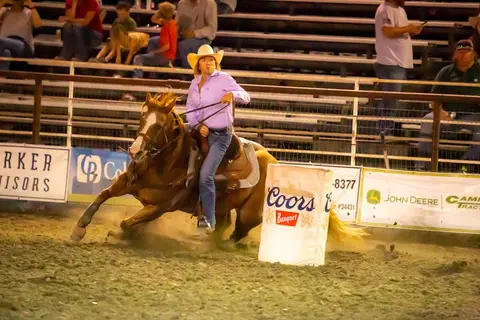 A woman rides a horse around a barrel in an arena.