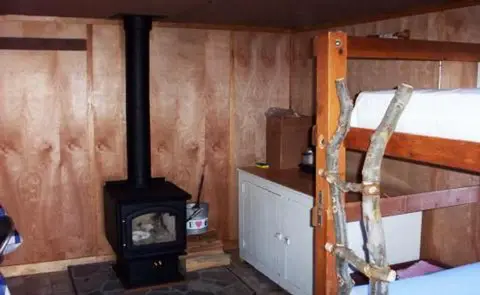 An interior view showing a wood-burning stove and bunk beds with rustic ladder posts.