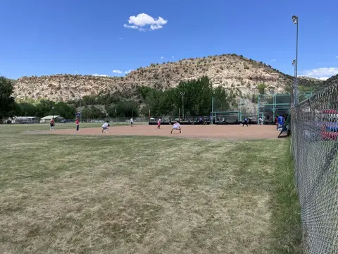 People playing baseball on a dirt field with a large rocky hill in the background.