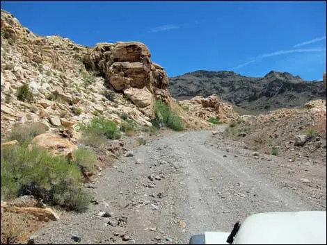 A dirt road winds through a rocky desert landscape under a clear blue sky.