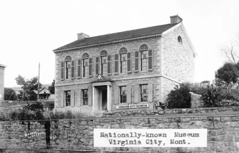 Black and white historic photo showing the exterior of a stone building with arched windows and shutters.