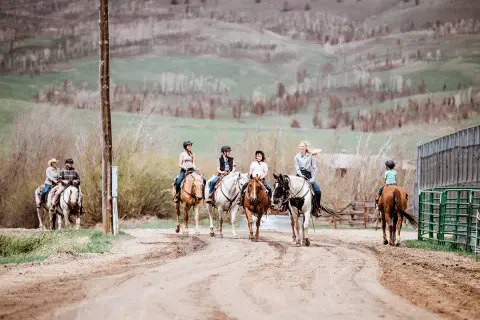 A group of people riding horses on a dirt path with hills in the background.