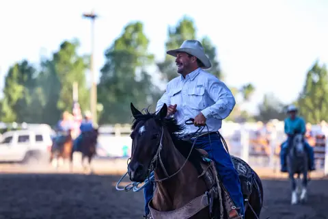A smiling cowboy rides a horse outdoors.