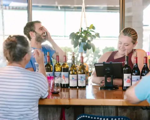 People interacting and laughing at a wine tasting counter inside a building.