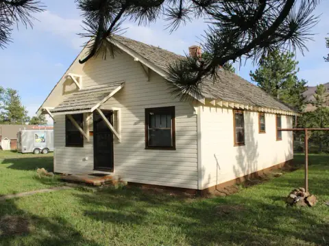 An exterior view of a small one-story yellow house with a shingle roof.