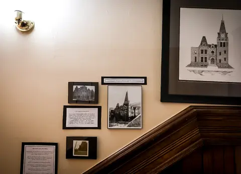 Framed historical photographs and a drawing of a building hang on a wall.