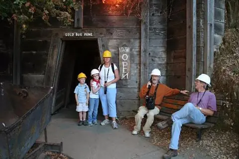 People wearing hard hats stand outside the entrance to a mine with an open sign.
