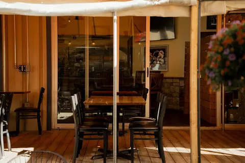 An outdoor patio dining area with wooden tables and chairs under a canopy.