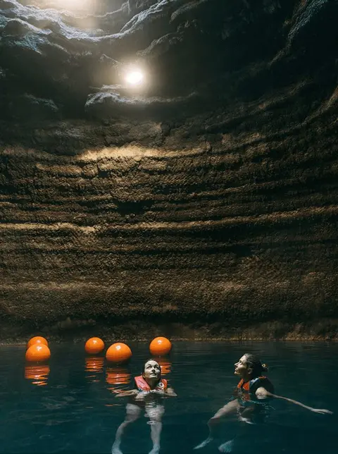 Two people swim in a body of water inside a cavern.