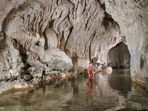 A person in a protective suit stands in an underground river inside a cave.