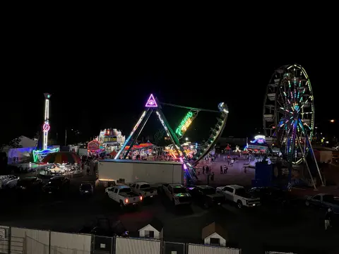 A brightly lit amusement park at night with rides and parked cars.