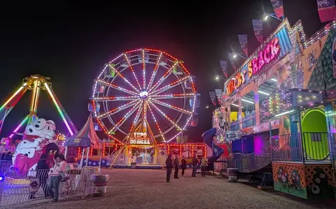 A brightly lit Ferris wheel and carnival rides at night.