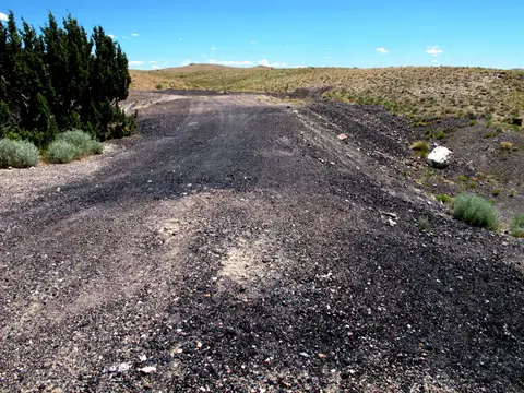 A dirt road winds through an arid, hilly landscape under a blue sky.
