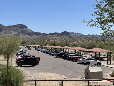 A parking lot with cars and picnic shelters against a mountain backdrop.