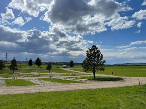 An open grassy landscape with dirt roads under a dramatic cloudy sky.