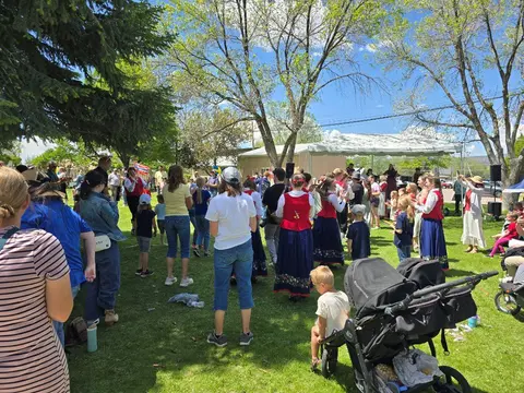 A crowd of people gathers in a grassy park to watch a performance.