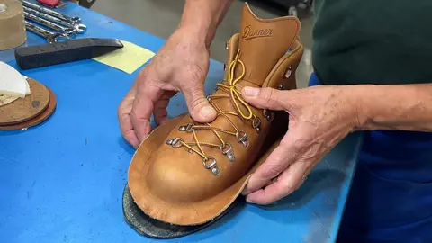 A person works on crafting a leather boot on a blue workbench.