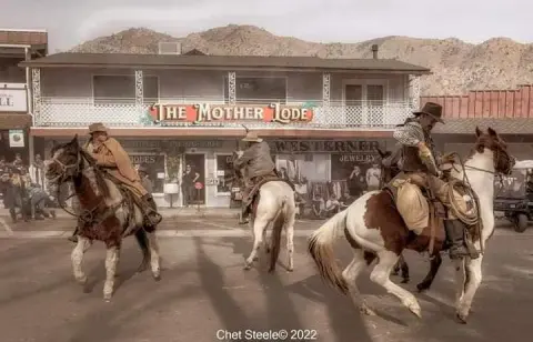 Three people on horseback in front of a Western-style building.