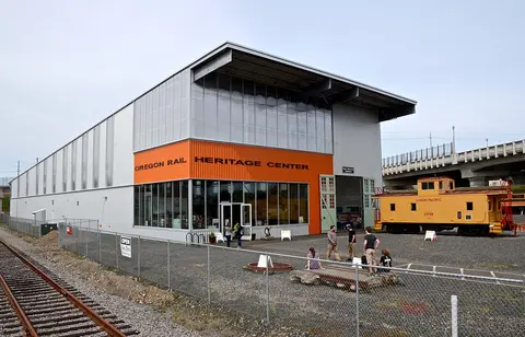 A modern industrial building with an orange sign and a train car parked outside.