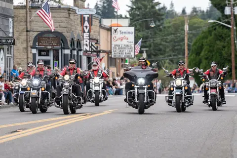 A group of motorcyclists ride in formation down a street during an event.