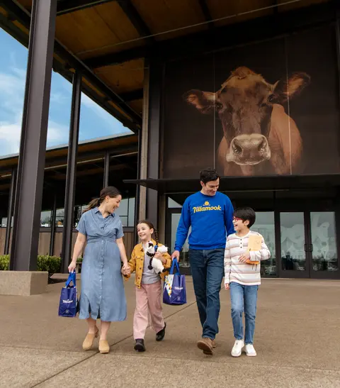 A family walks outside a modern building with a large cow graphic on the wall.