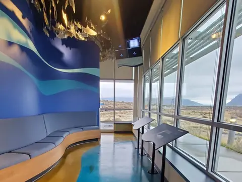 An interior view of a room with a curved blue seating area and large windows overlooking an outdoor landscape.