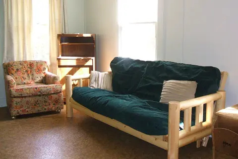 An interior shot of a living room with a wooden futon and a patterned armchair.