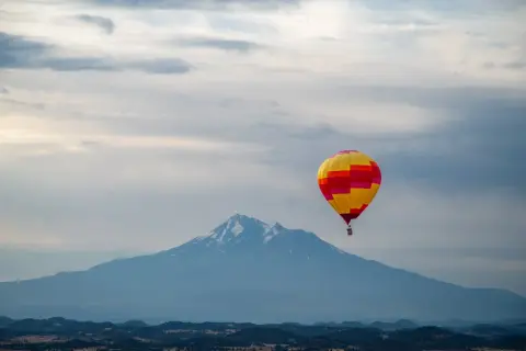 A hot air balloon flying over a landscape with a large mountain in the background.