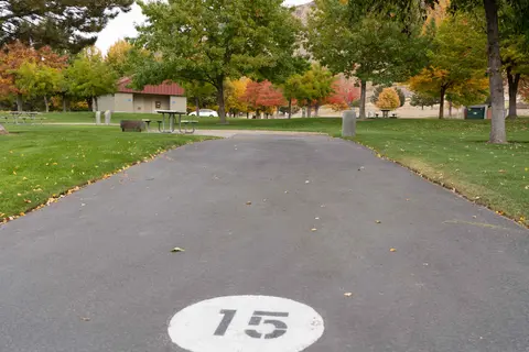 An asphalt path with the number 15 painted on it leads through a park with autumn trees.