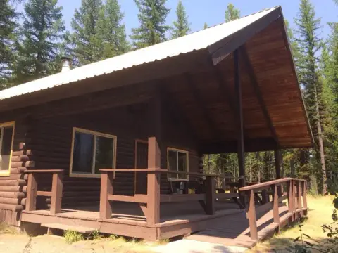 A wooden cabin with a porch and ramp surrounded by trees.