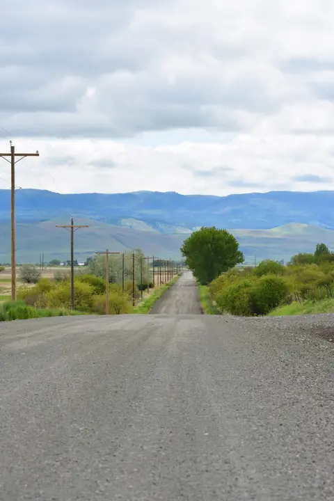 A gravel road stretches toward distant mountains under a cloudy sky.