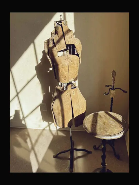 A vintage adjustable dress form and a small decorative table stand in an indoor room.