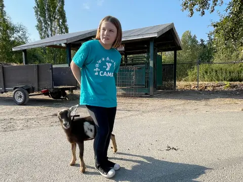 A young girl standing outside with a small goat.