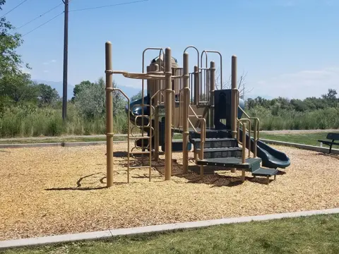 A modern playground structure stands on a bed of wood chips outdoors.