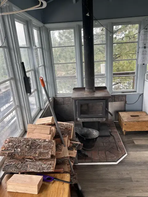 A wood-burning stove sits in the corner of a sunroom with large windows.