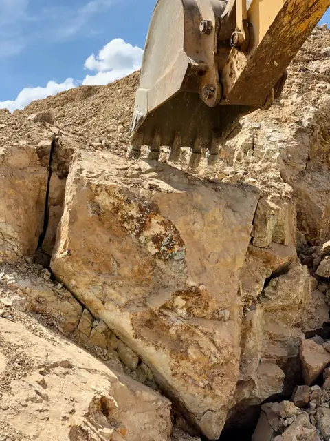 An excavator bucket digging into rock.