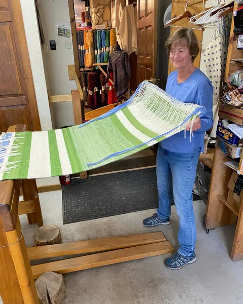 A woman holds up a woven textile inside a shop.