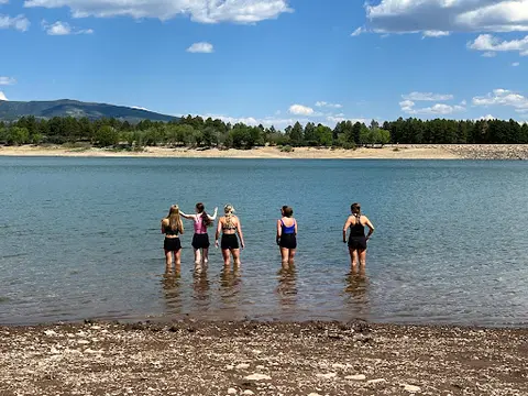 Five people stand in shallow water facing a lake.
