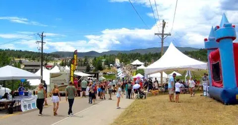 A crowd of people enjoying an outdoor festival with tents and a bounce house.