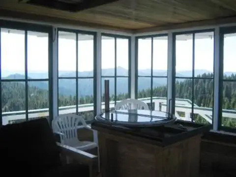 The interior of a wooden structure with large windows overlooking a forested mountain landscape.