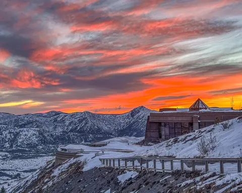 A snow-covered landscape and building beneath a vibrant red and orange sunset sky.