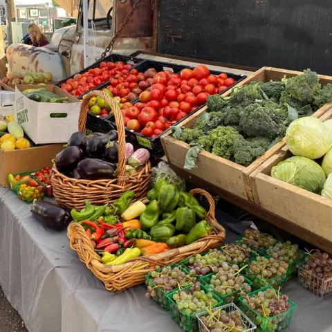 A stand displays fresh produce including tomatoes, peppers, broccoli, and grapes.