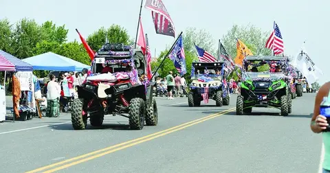 Decorated off-road vehicles drive down a street during a community parade.