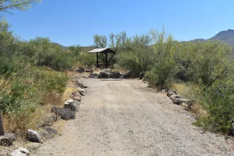 A dirt path leads to a covered picnic shelter in a desert landscape.