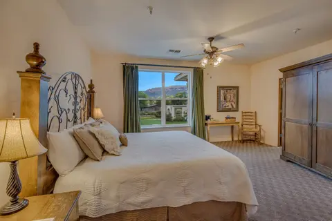 A well-lit bedroom with a large bed, wooden furniture, and a window looking out to a landscape.