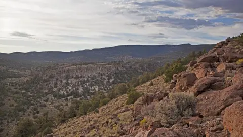 A rocky landscape with hills and sparse vegetation under a cloudy sky.