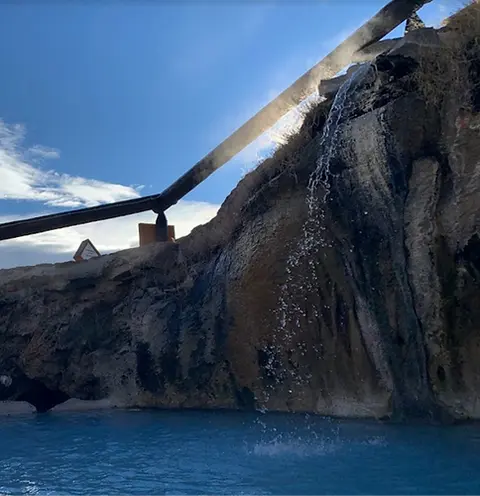 A small waterfall flows from a rocky cliff into a blue pool of water below.